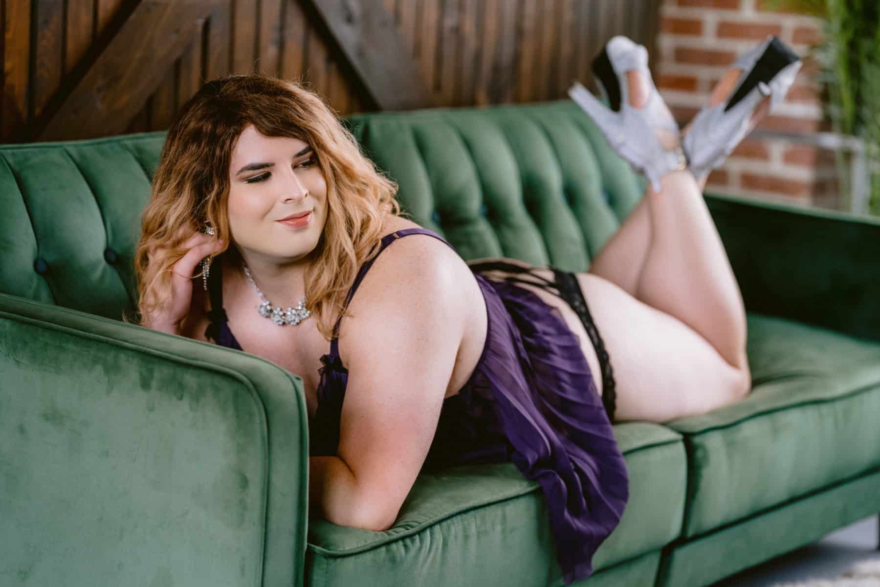 Trans woman poses confidently on green velvet couch during gender affirming boudoir session