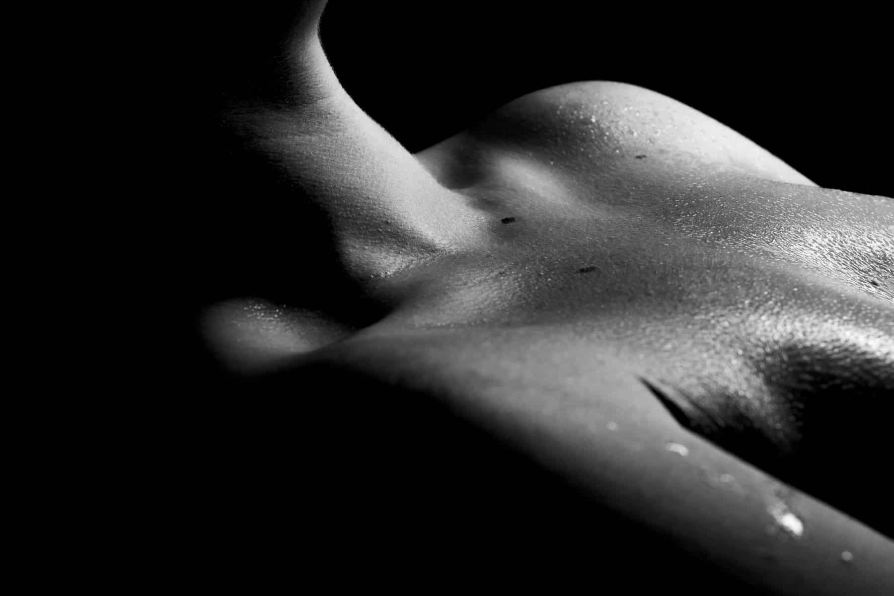 A black and white bodyscape image of a woman's wet skin, focusing on her neck and collarbone and cleavage.