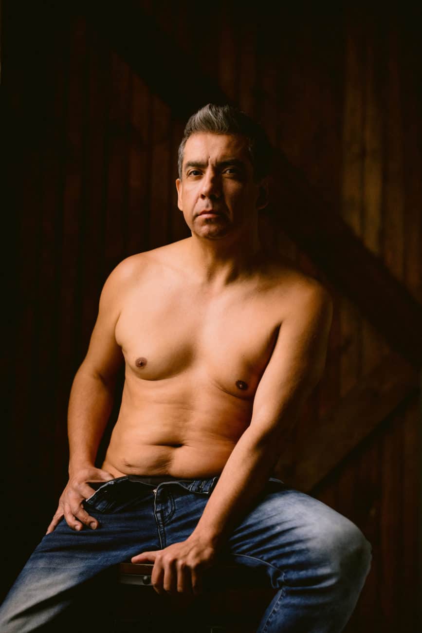 Man standing near a window during a boudoir session, embracing the thrill of being seen.