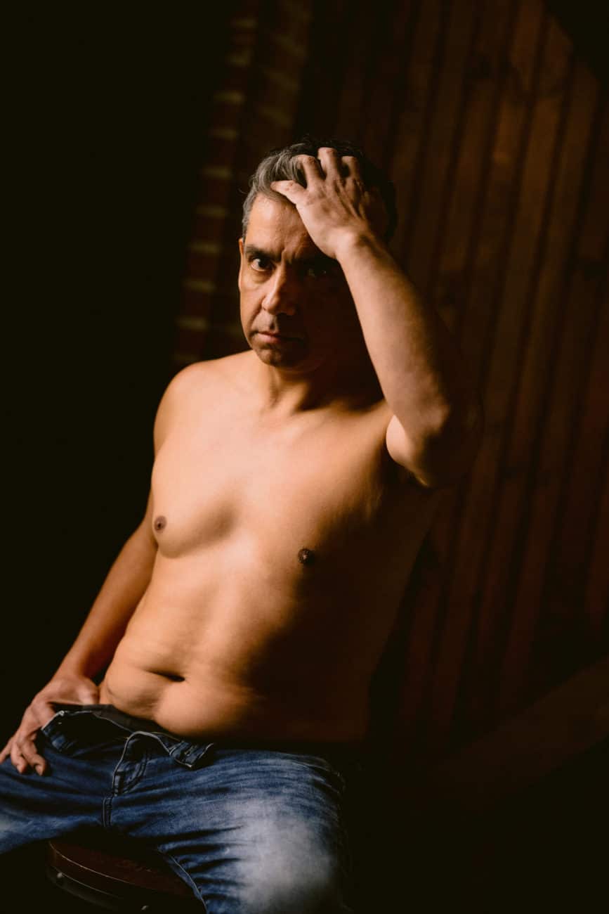 Man standing near a window during a boudoir session, embracing the thrill of being seen.