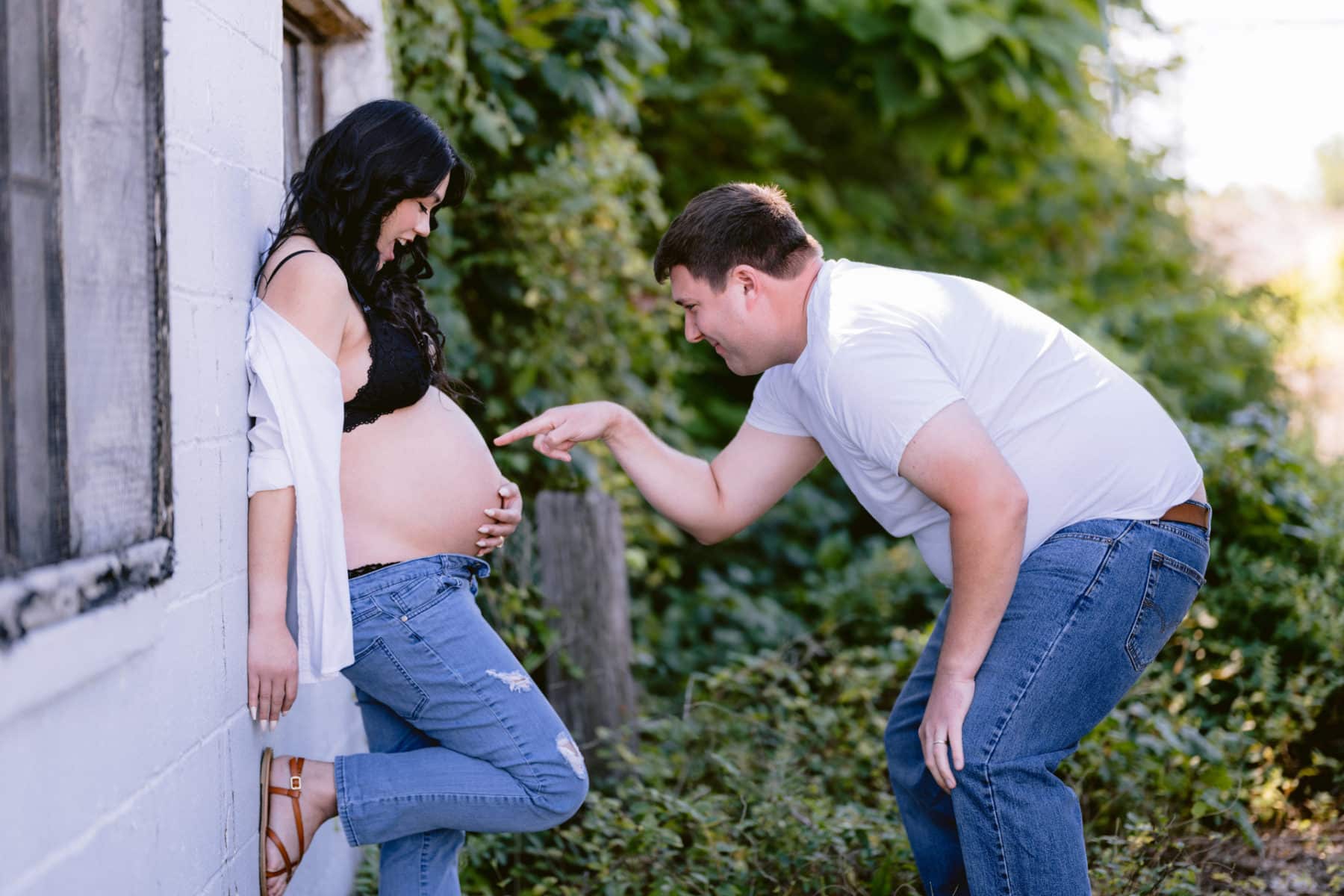 Dad to be poking wife's pregnant belly, outside, cute and playful.